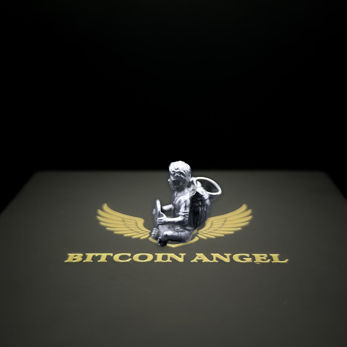 Amulet of an angel holding a Bitcoin symbol with 'Bitcoin Angel' text on a dark background