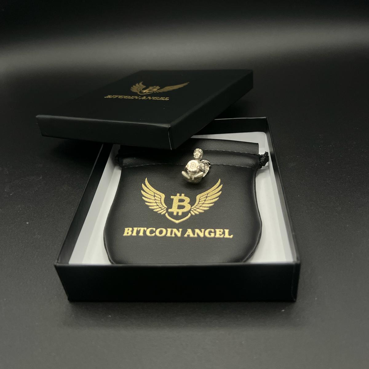 Bitcoin Angel figurine in a black box with gold logo on a dark background